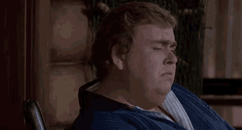 a man in a blue sweater is sitting in a chair and making a sad face .