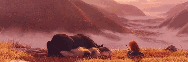 a wolf is sleeping in a field with mountains in the background and a girl is standing next to it .