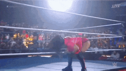 a woman in a red shirt is kneeling down in a wrestling ring with a live sign above her