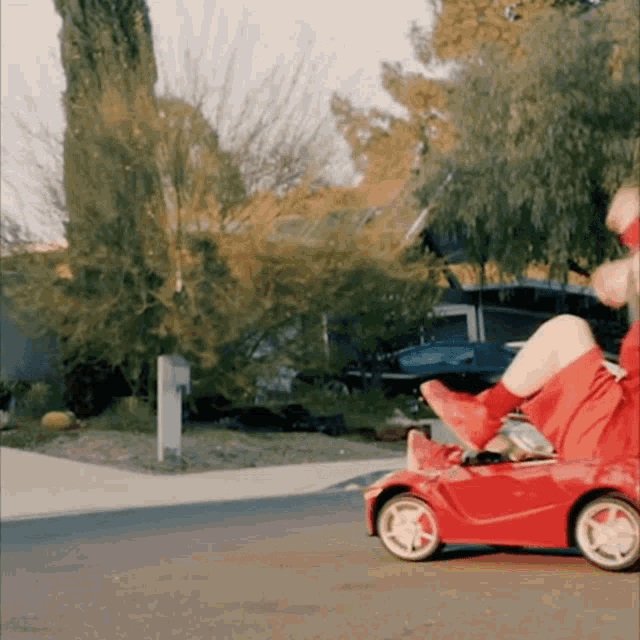 a person riding a red toy car on a street