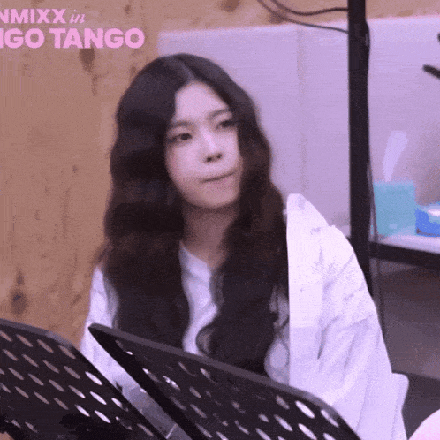 a girl with long black hair is sitting in front of a sign that says nmixx in go tango