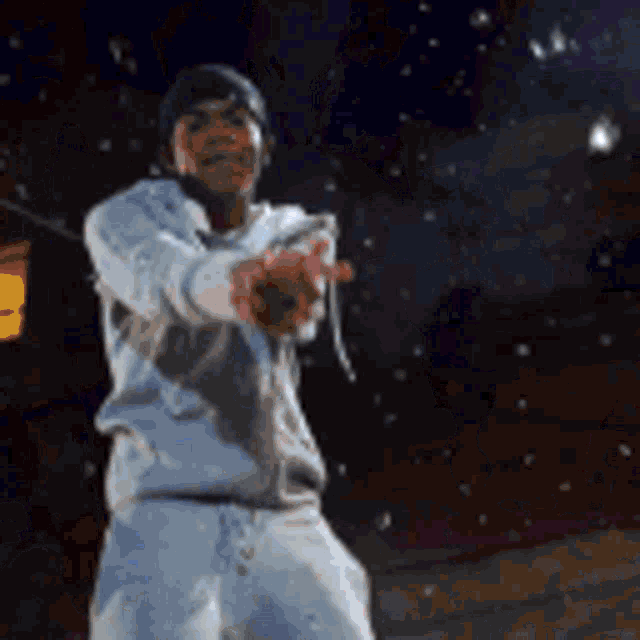a man in a white sweatshirt and white shorts is pointing at the camera at night .