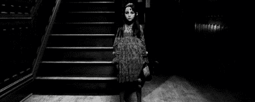 a black and white photo of a scary little girl walking down a set of stairs .