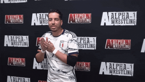a wrestler stands in front of a wall that says alpha 1 wrestling