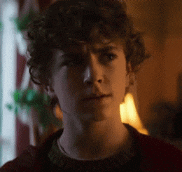 a young man with curly hair is wearing a red sweater .