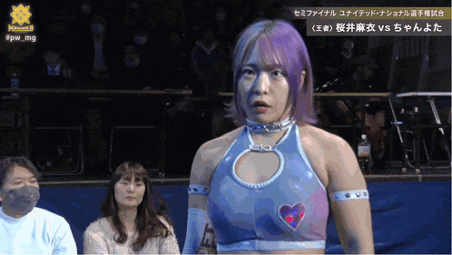 a woman in a blue top with a heart on the chest is standing in front of a crowd