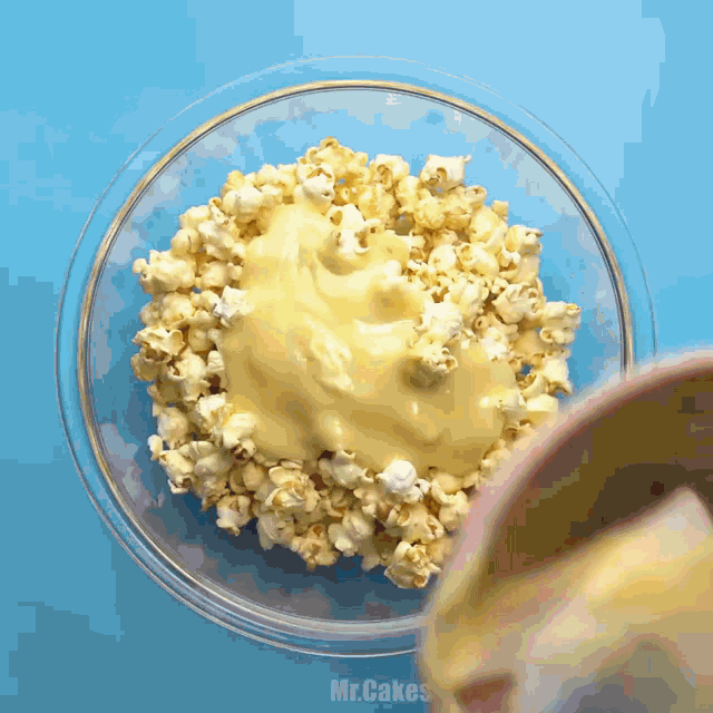 a bowl of popcorn is being poured into a bowl of cheese sauce by mr.cakes