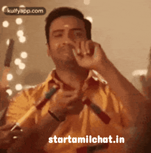 a man in a yellow shirt is holding a microphone in his hand and says starttamilchat.in
