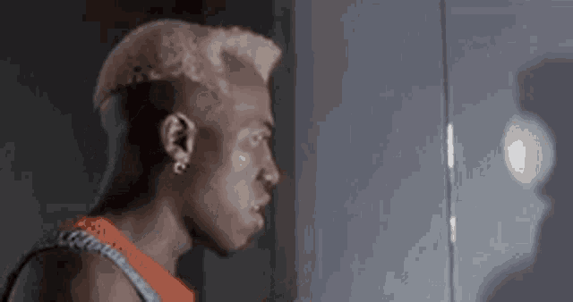 a man with a shaved head is looking at himself in a mirror .