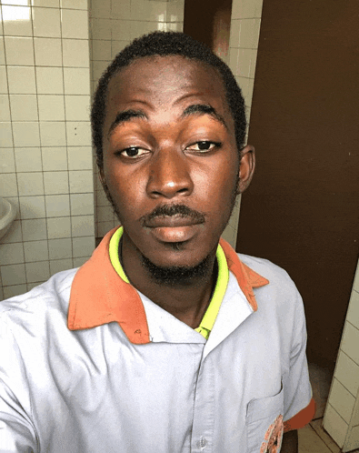 a man wearing a white shirt with a yellow collar looks at the camera