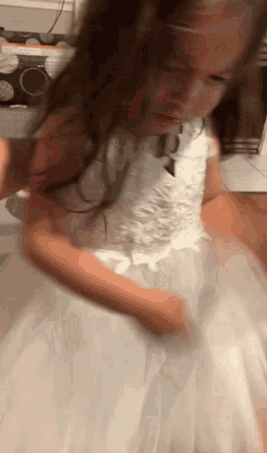 a little girl in a white dress is playing with her hair