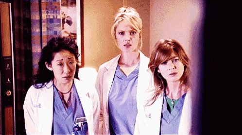 three women in scrubs and lab coats are standing next to each other in a hallway .
