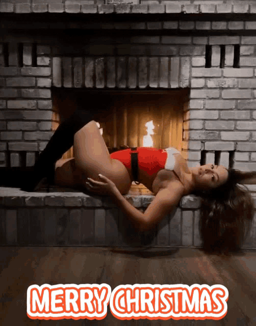 a woman in a santa outfit is laying in front of a fireplace and the words merry christmas are above her