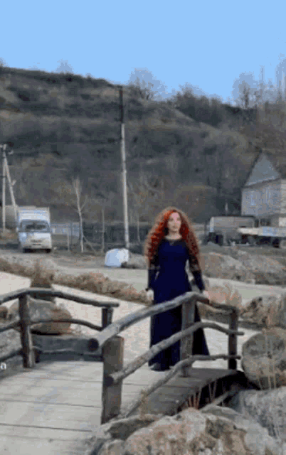 a woman in a blue dress stands on a bridge