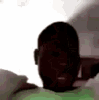 a man in a green shirt is laying on a bed and making a funny face .