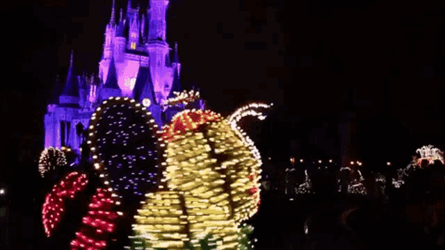 a group of people are dancing in front of a castle at a disneyland christmas parade .