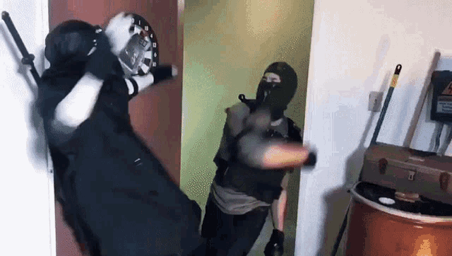 a man in a black mask is holding a dart board and another man in a black mask is holding a gun
