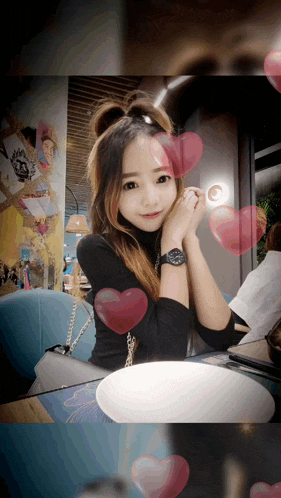 a woman wearing a watch is sitting at a table with hearts around her