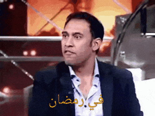 a man in a suit is sitting in front of a sign that says ' ramadan ' on it