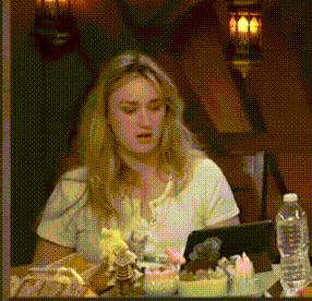 a woman in a white shirt is sitting at a table with a tablet and a water bottle .