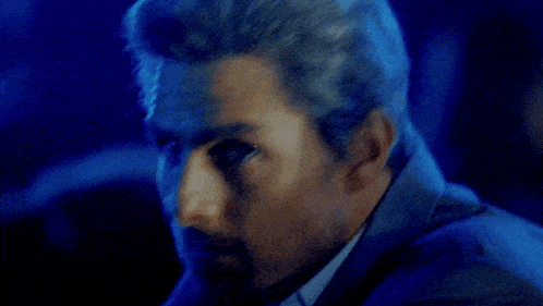 a man in a suit and tie is looking at the camera with a blue light behind him .