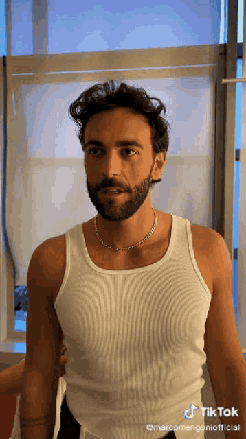 a man with a beard is wearing a white tank top and a tiktok video