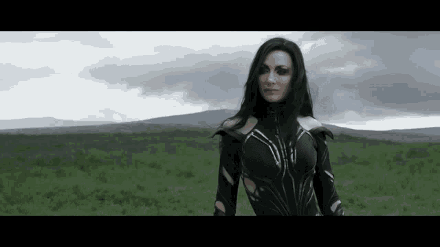 a woman in a superhero costume is standing in a field with mountains in the background .