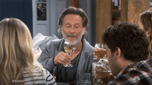 a man with a beard is holding a glass of wine while sitting at a table with other people