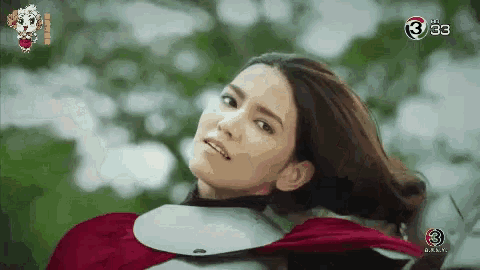 a woman is wearing a red cape and armor and looking at the camera .