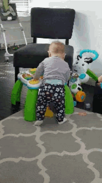 a baby is standing on a rug next to a toy table