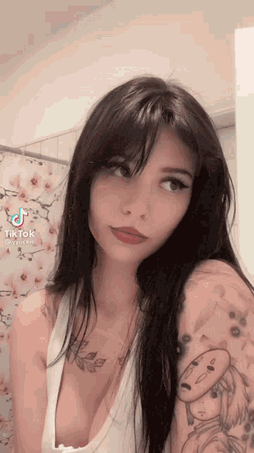 a woman with a tattoo on her arm is looking at the camera with a tik tok sticker on her face