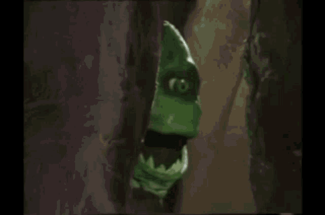 a green monster with sharp teeth is standing in a dark room .