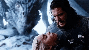 a man and a woman are laying in the snow with a dragon behind them .