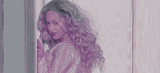 a woman with long blonde curly hair is standing next to a door .