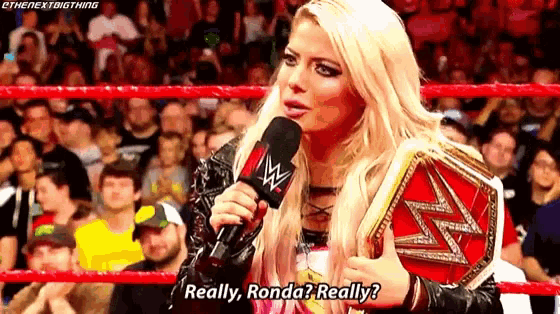 a woman is holding a wrestling championship belt and talking into a microphone in a ring .