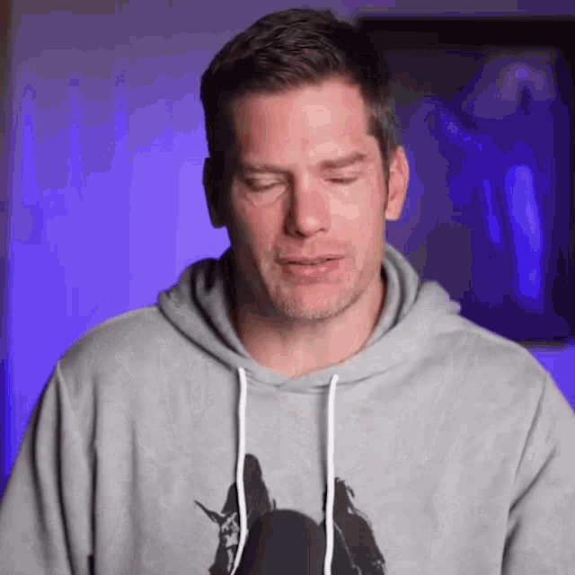a man wearing a gray hoodie with a silhouette of a person on it is making a funny face .