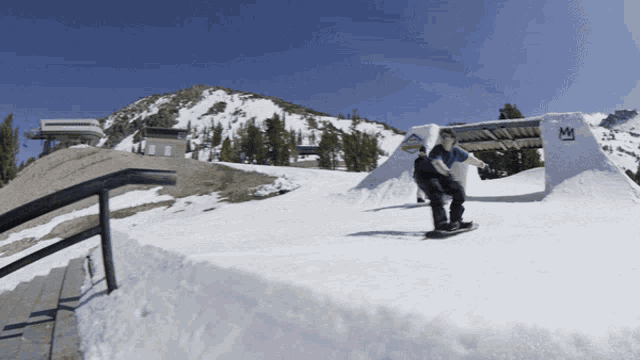 a snowboarder is doing a trick on a snowy ramp with a sign that says m on it