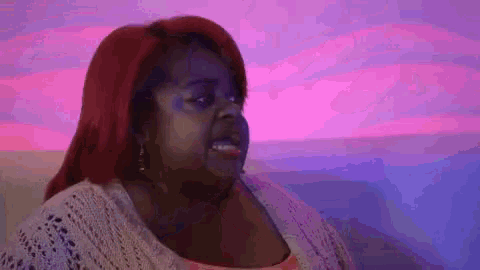 a woman with red hair is making a funny face in front of a purple and pink background .
