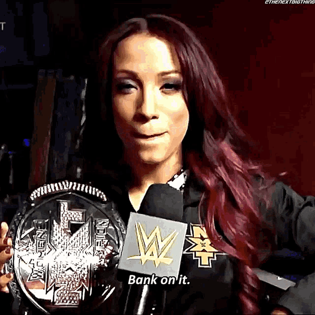 a woman with red hair is holding a wrestling championship and talking into a microphone saying bank on it
