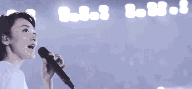 a woman in a white shirt is singing into a microphone on a stage .