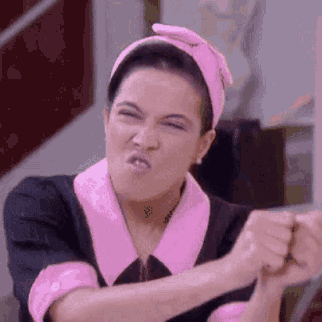 a woman wearing a pink headband and a pink dress is making a funny face .