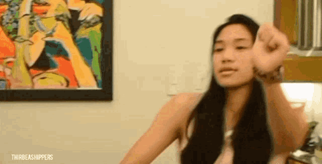 a woman is giving a thumbs down sign in front of a painting on the wall .