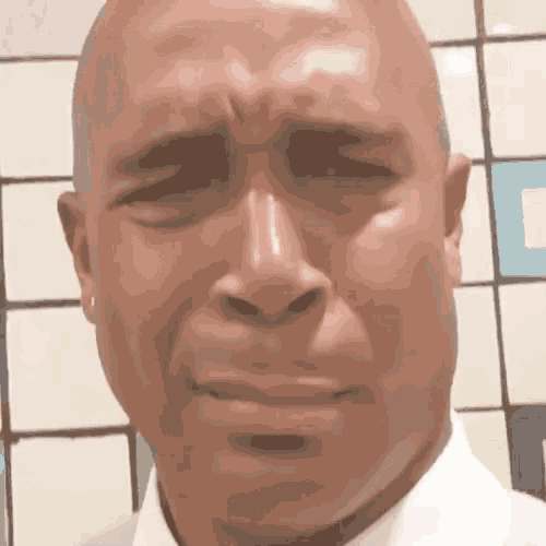 a bald man is crying in front of a tiled wall .