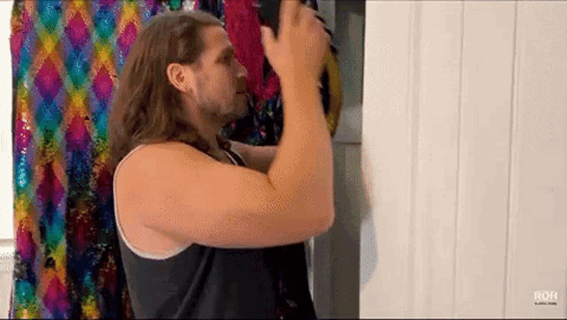a man with long hair and a beard is standing in front of a colorful curtain in a closet .