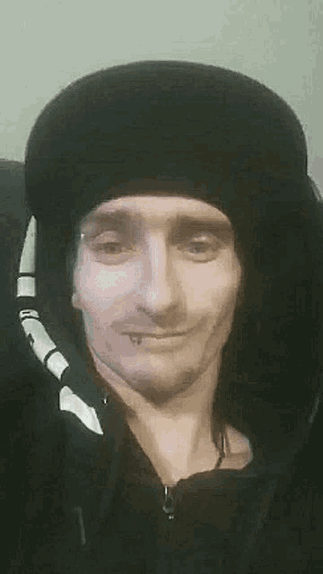 a man wearing a black hat and hoodie is smiling .