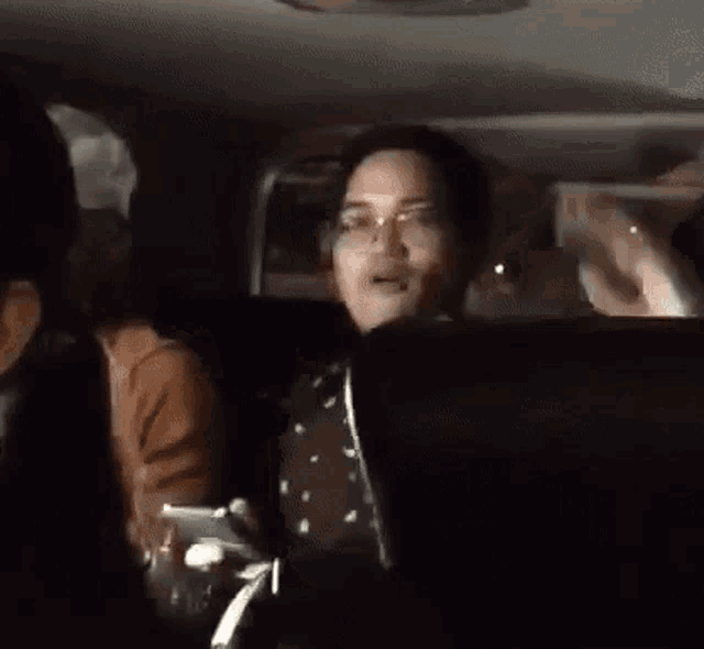 a woman wearing glasses is sitting in the back seat of a car with her hand in the air .
