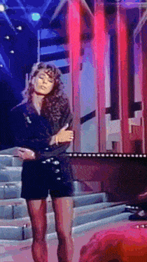 a woman with curly hair is standing on a stage in front of a red light