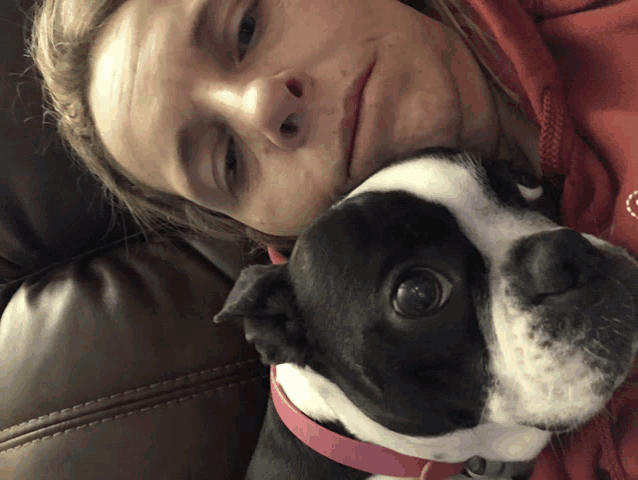 a woman laying on a couch with a black and white dog on her lap