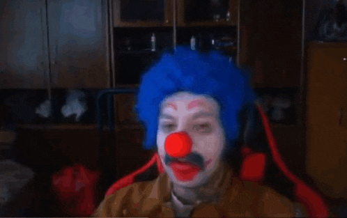a man wearing a blue wig and a red nose is sitting in a chair .