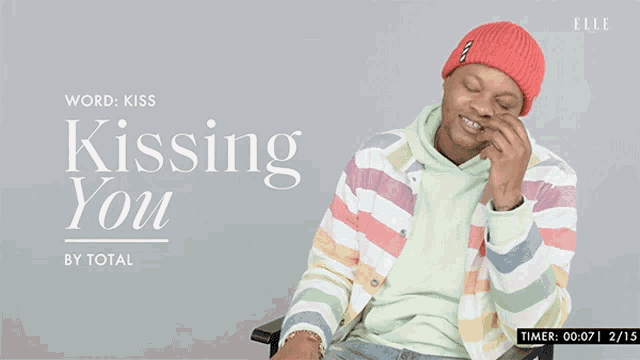 a man wearing a striped jacket and a red hat is sitting in front of a sign that says kissing you by total